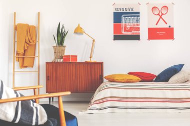 Sarı lamba ve bitki spor yatak odası iç posterler ile yatakta yanında ahşap dolap üzerinde. Gerçek fotoğraf