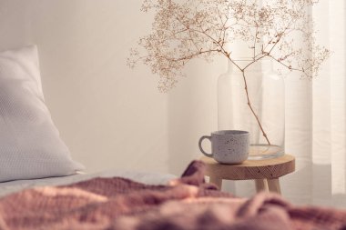 Kahve fincanı ve parlak yatak odası iç, gerçek fotoğraf kopya alanı boş duvar ile başucundaki cam vazoda çiçek closeup
