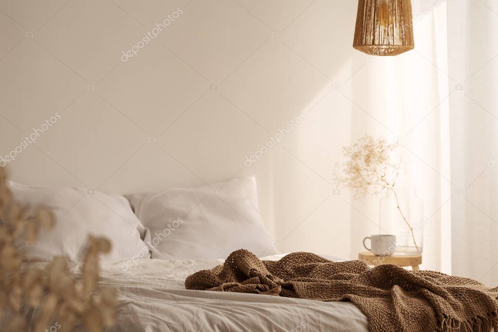 Rattan chandelier above king size bed with white bedding and beige blanket, real photo
