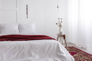 Küçük ahşap masa sonraki toking boyutu yatak beyaz yatak ve kırmızı battaniye, kopya alanı boş duvar ile gerçek fotoğraf ile rustik metal vazo içinde kahve Kupası ve pamuk çiçek