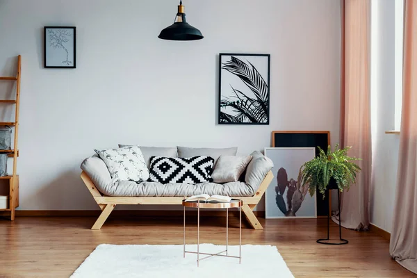 stock image Patterned black and white pillow on beige scandinavian sofa in stylish interior with gallery of poster on the wall and white carpet on wooden floor, real photo