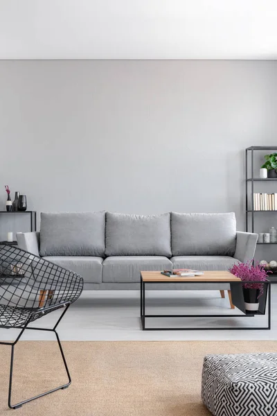 Real photo of a simple living room interior with a grey sofa, armchair, coffee table and brown rug. Empty wall, place your graphic