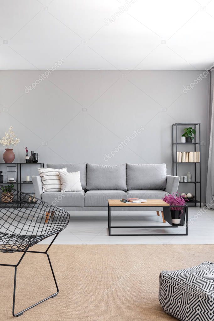 Vertical view of elegant grey living room with comfortable couch, metal shelves and wooden coffee table, real photo with copy space