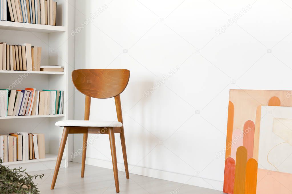 Wooden chair and poster in simple white living room interior with books on shelves. Real photo