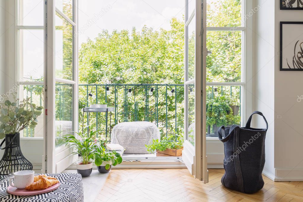 Green plants in pots in open door to balcony with small stylish table and pouf, real photo