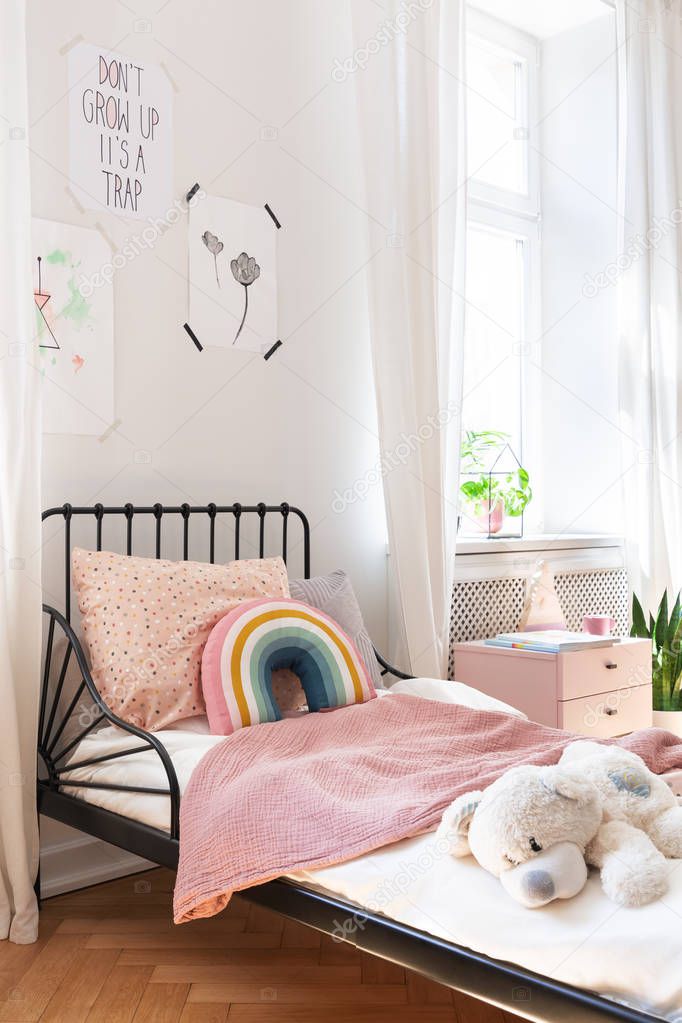 Pink bedding and teddy bear on small kids bed in stylish bedroom of elegant apartment