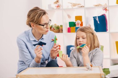 Mother holding toys while playing with daughter at girl's room clipart