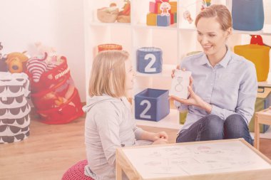 Smiling psychotherapist showing picture of ring during therapy with autistic girl clipart