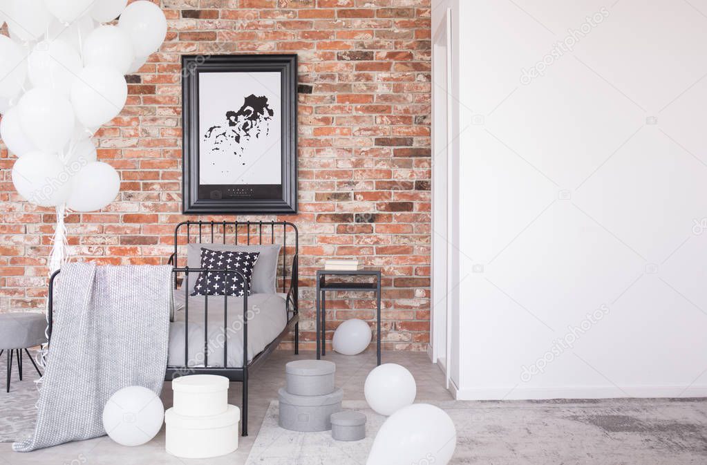 Poster on red brick wall above grey bed in bedroom interior with copy space and balloons. Real photo