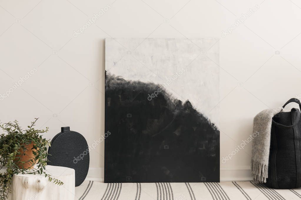 Black and white painting between black basket with grey blanket and black vase, patterned carpet on the floor