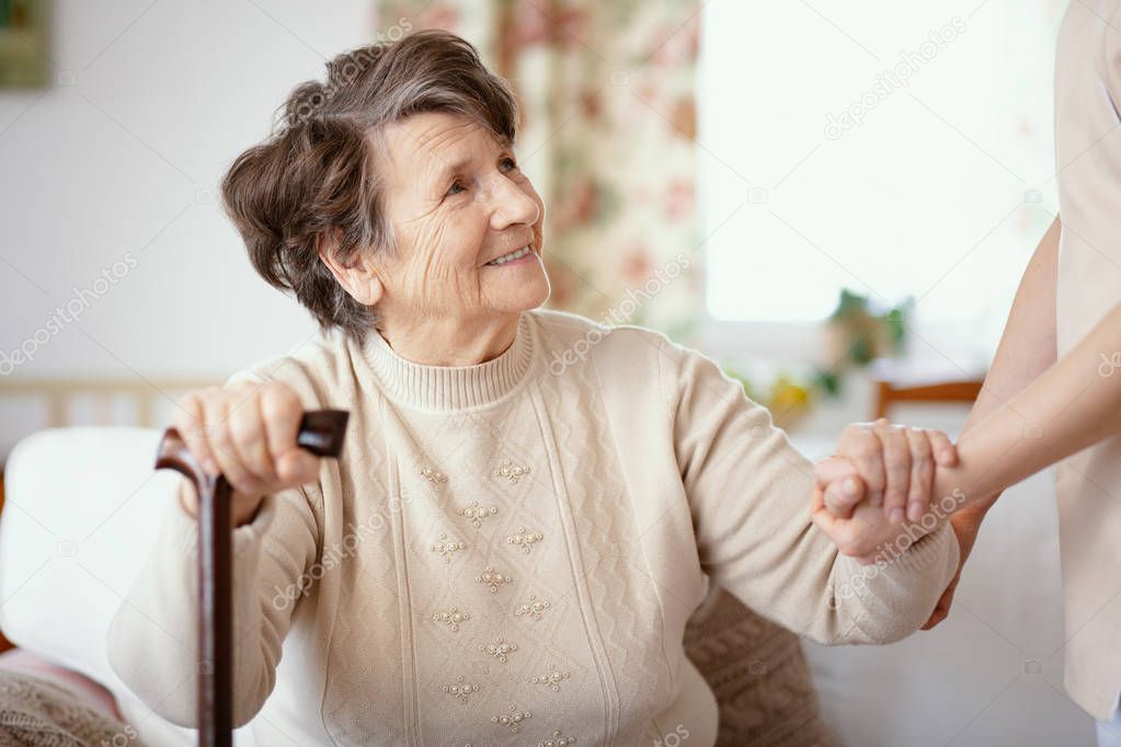 Smiling senior woman with walking stick and helpful caregiver holding her hand