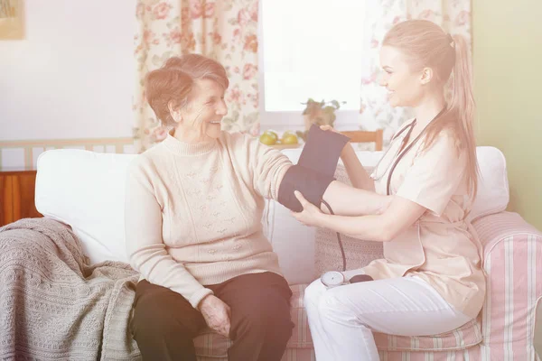 Smiling doctor measuring pressure of happy senior woman at home