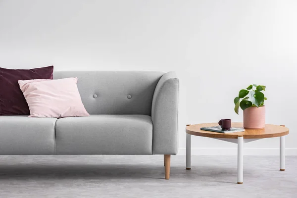 种植在木桌旁边的灰色沙发与粉红色和紫色的枕头在灰色阁楼内部 真实照片 — 图库照片