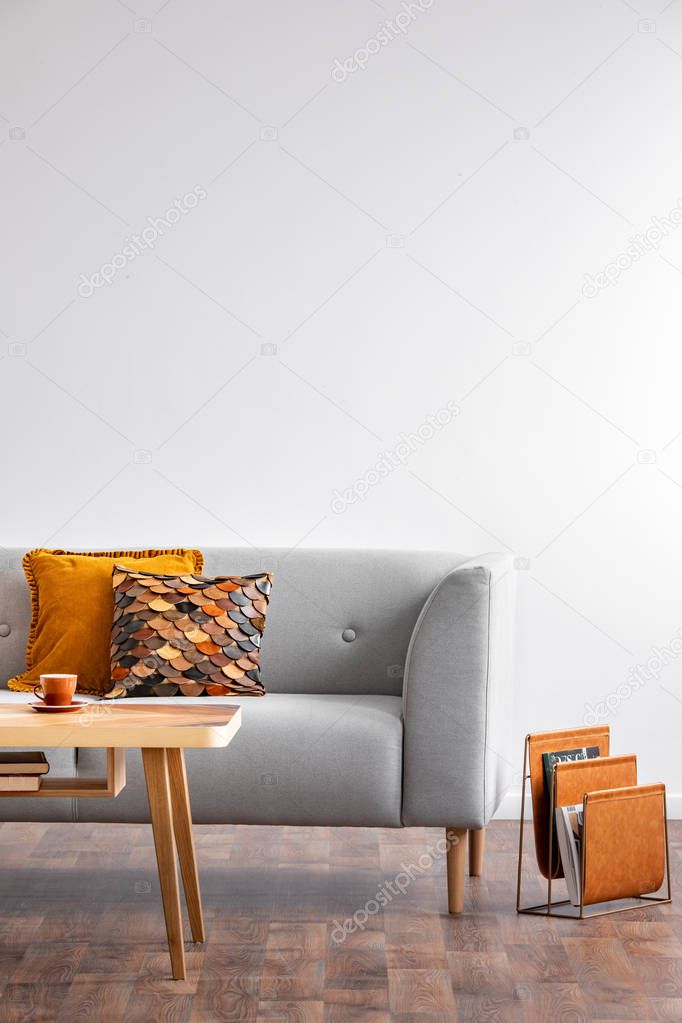 Coffee table with cup in bright scandinavian living room interior with grey couch and autumn color pillows, real photo with copy space on the empty wall