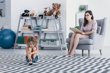 Üzgün ve yalnız çocuk ve psikoterapist ofiste tedavi sırasında