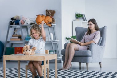 Bir çocuk bir tablo tarafından oturan ve bir oyuncak ayı bir aile destek merkezindeki bir terapist ile tedavi edici bir toplantı sırasında isabet davranış sorunları ile.