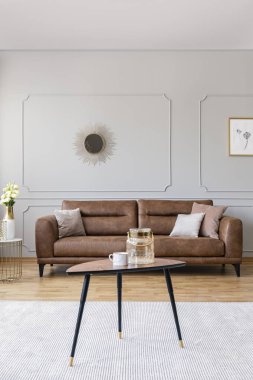 Zarif salon iç deri kanepe, altın ayna ve ahşap zemin ile gerçek fotoğraftaki beyaz halı üzerinde çay kupa ve cam vazo konumu olan ahşap masa