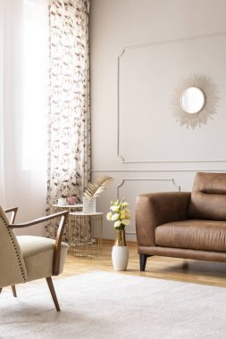 Real photo of bright living room interior with white carpet, window with curtains and fresh roses in vase placed by leather brown sofa