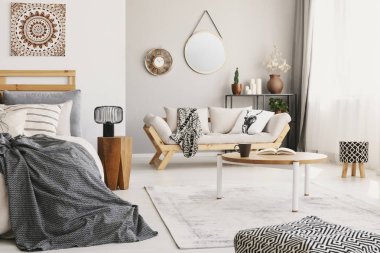 Yatak, perdeler ile pencere, sehpa ile kupa ve halı üzerinde yerleştirilen kitap ile küçük düz iç salon, battaniye ve yastık ve saat ve gerçek fotoğraf duvardaki ayna