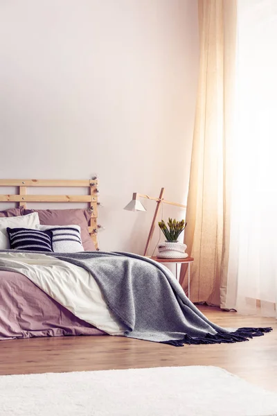 キングサイズ木製ベッドの上の汚れたピンクのシート コピー領域を実際の写真でグレーの居心地のよい毛布 パターン化された枕の垂直ビュー — ストック写真
