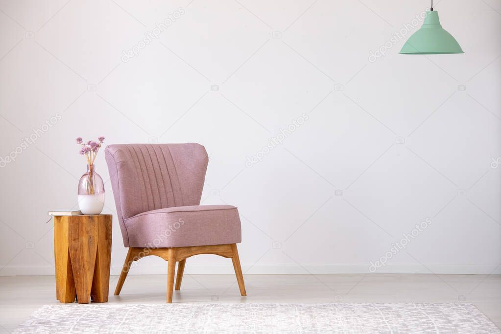 Flowers on wooden stool next to pink armchair in flat interior with copy space and mint lamp. Real photo