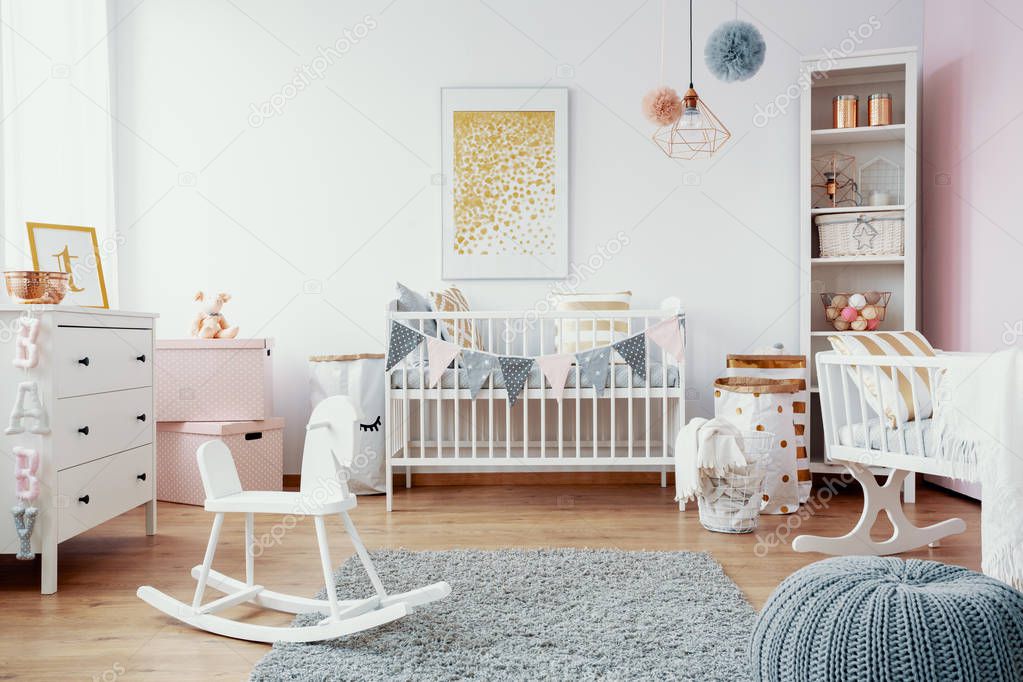 Bright baby room with white furniture, grey carpet on the floor and golden painting on the empty wall, real photo