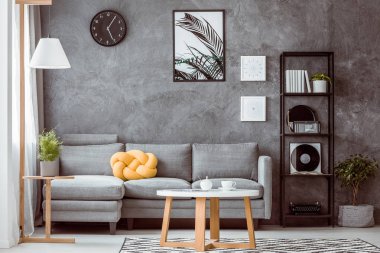 Gri beton duvar endüstriyel siyah metal bookshelf yanındaki sarı düğüm yastık ile rahat kanepe ile modern oturma odasında