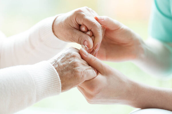 Closeup of the hands of a young woman holding hands of an elderly lady