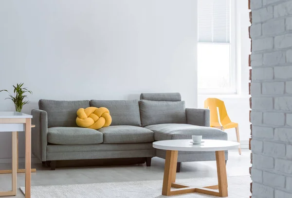 黄色的结枕头在灰色角落沙发上明亮的客厅与圆形的白色木咖啡桌 复制空间在空的白色墙壁 — 图库照片