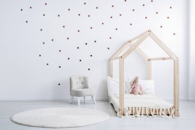 Oyuncak ve battaniye, kopya alanı ve boş beyaz duvar, altın yıldız ahşap ev şekli yatak yanında pastel gri tekli yuvarlak zemin üzerinde beyaz halı