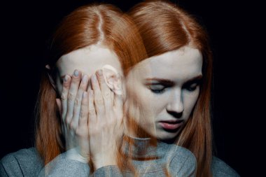 Porter of beautiful redhead girl with psychotic disorders covering her face, hiding from her hallucinations, black background behind her clipart