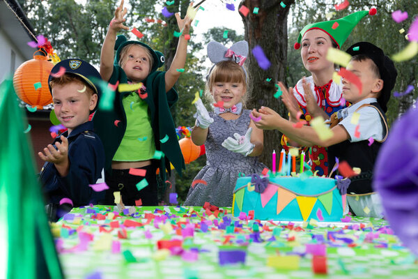 Smiling children wearing carnival costumes have fun during birthday party with cake