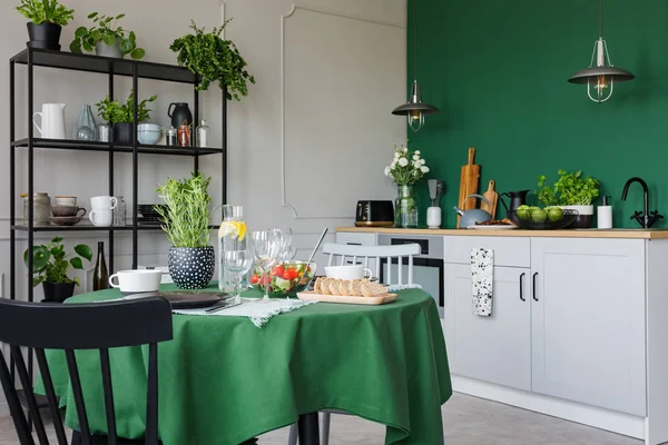 Trendy kitchen with dining table with green tablecloth set for romantic dinner