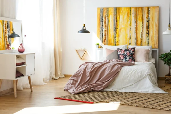 花枕头和柔和的粉红色床单在国王大小的床上 在当代卧室的内部 墙上有花哨的绘画 木地板上有天然的地毯 — 图库照片