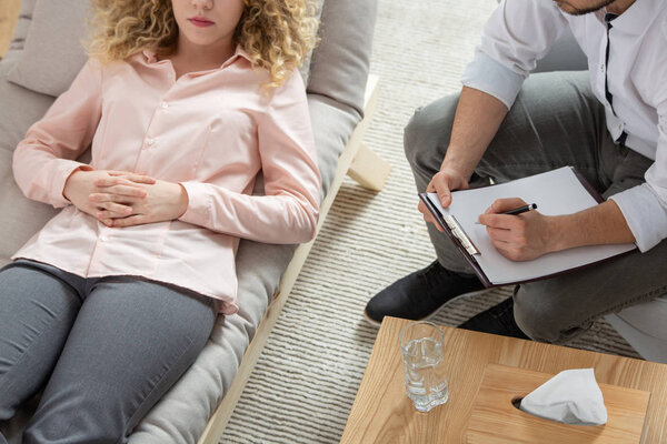 Young woman with anxiety and panic disorder laying on settee during meeting with her psychiatrist