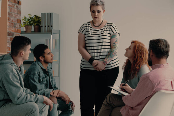 Sad teenage girl with tattoos talking about problems during meeting of support group