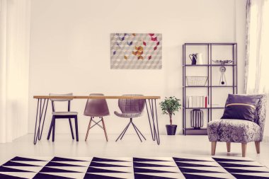 Gri koltuk ve aydınlık yemek salonunda saat ve duvardaki poster ve yerdeki bitki ile geometrik halı yastık