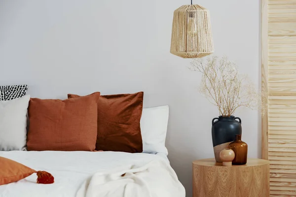 棕色枕头在白色床在自然卧室内部与柳条灯和木制床头柜与花瓶 — 图库照片