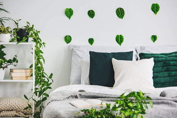 Closeup of green leafs on white wall of elegant bedroom interior king size bed with green and white bedding