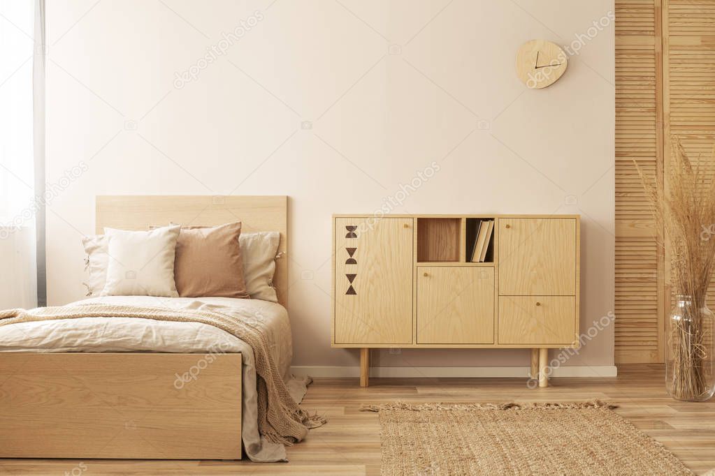 Single wooden bed with beige bedding and blanket next to stylish wooden cabinet in elegant bedroom