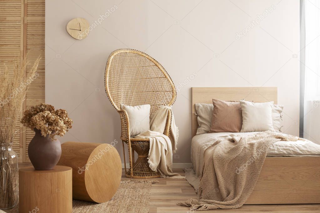 Peacock chair with pillow and blanket next to single bed with beige bedding and warm blanket, real photo