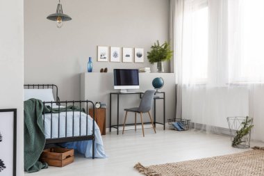 Parlak genç yatak odası tek kişilik metal yatak, gri sandalye ve küre ve bilgisayar ile endüstriyel resepsiyon ile boş gri duvar grafik