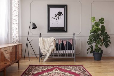 Persian carpet on the floor of mid century baby room interior with grey wooden crib, industrial black lamp and monster plant in pot clipart