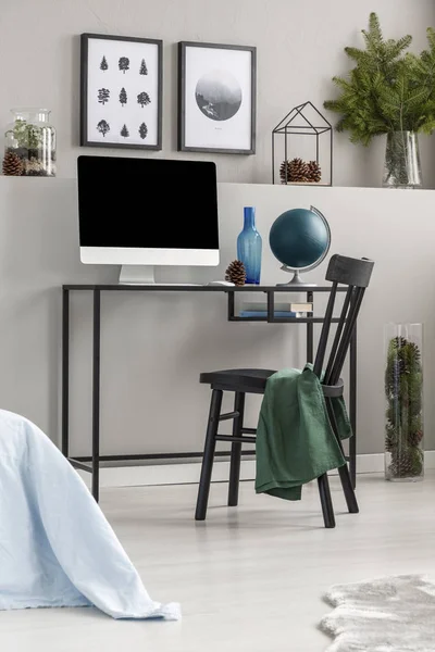 Brunches of spruce in glass vase above desk with computer and globe in elegant forest inspired workspace interior