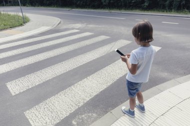 Yolun yanındaki yaya geçidi, bir smartphone konumu olan çocuk