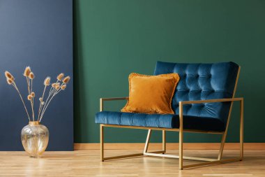 Brown cushion on blue armchair in green living room interior with flowers in gold vase. Real photo clipart