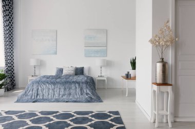 ' Beyaz şık yatak odası iç desenli halı ve posterler mavi yatak yukarıda tabloda bitki. Gerçek fotoğraf