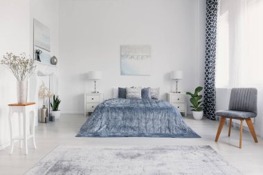 Mavi beyaz yatak odası iç posterler ve dolapları üzerinde lambalar ile yatakta yanındaki gri sandalye. Gerçek fotoğraf