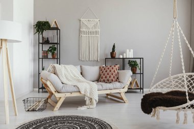 Handmade macrame on the empty wall of bright beige living room with comfortable couch with pillows and white blanket , real photo clipart