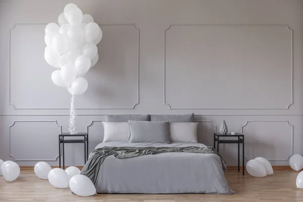 宽敞的卧室里有白色的气球 有特大号床 有灰色的羽绒被和黑色床头柜之间的枕头 在空荡荡的灰色墙壁上有复制空间的真实照片 — 图库照片